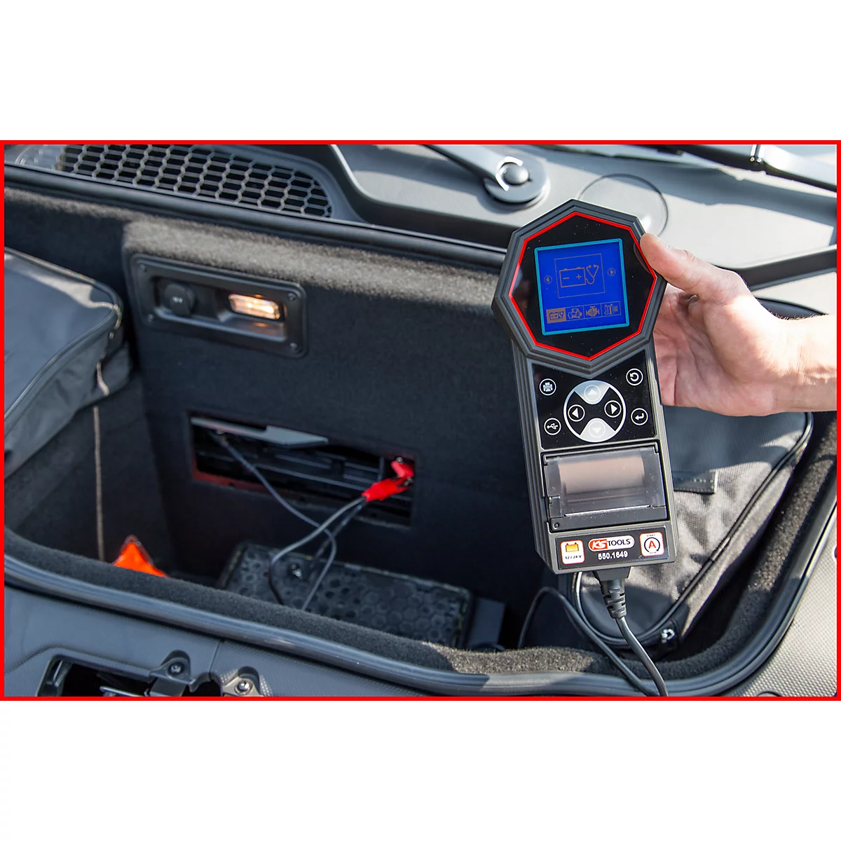 Person hält ein Diagnosegerät in der Hand, das im Kofferraum eines Autos verwendet wird. Der Bildschirm zeigt Messwerte an.